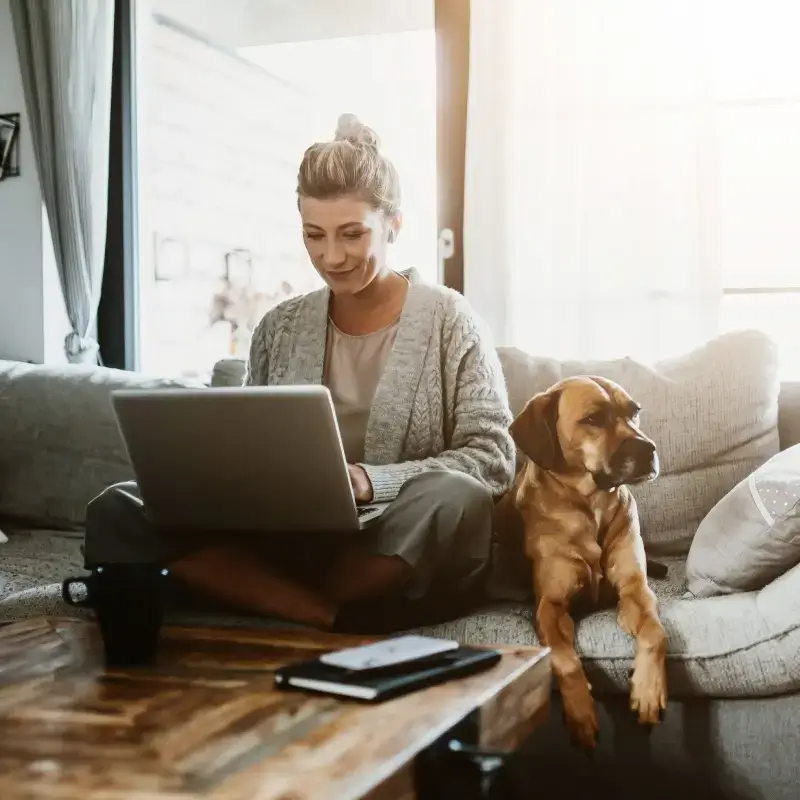 Woman working on laptop with her dog sitting beside her